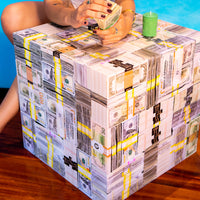 A person sitting next to a cube-shaped money table that is designed to resemble stacks of US currency.