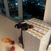 Stack of money with high-heeled shoes on a surface near a window with a cityscape view at night.