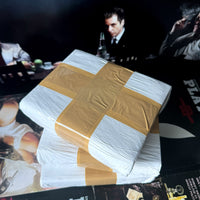 Stack of white prop cocaine bricks wrapped and sealed, displayed on a surface with blurred images of people in the background.