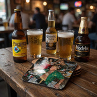 Three beer bottles and two glasses of beer on a wooden table with a colorful coaster underneath.